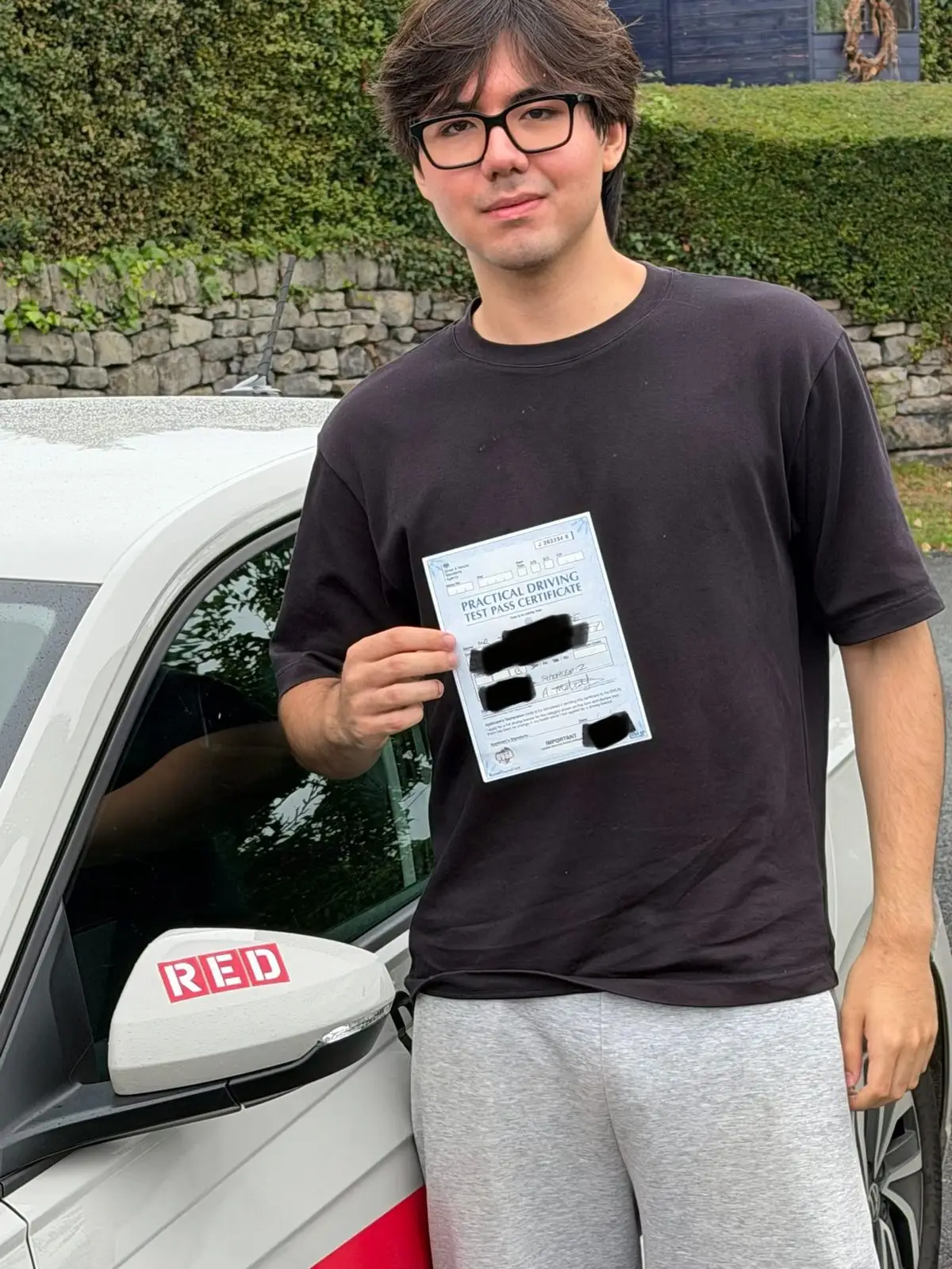 A learner holding their driving test pass certificate next to Mick&rsquo;s car