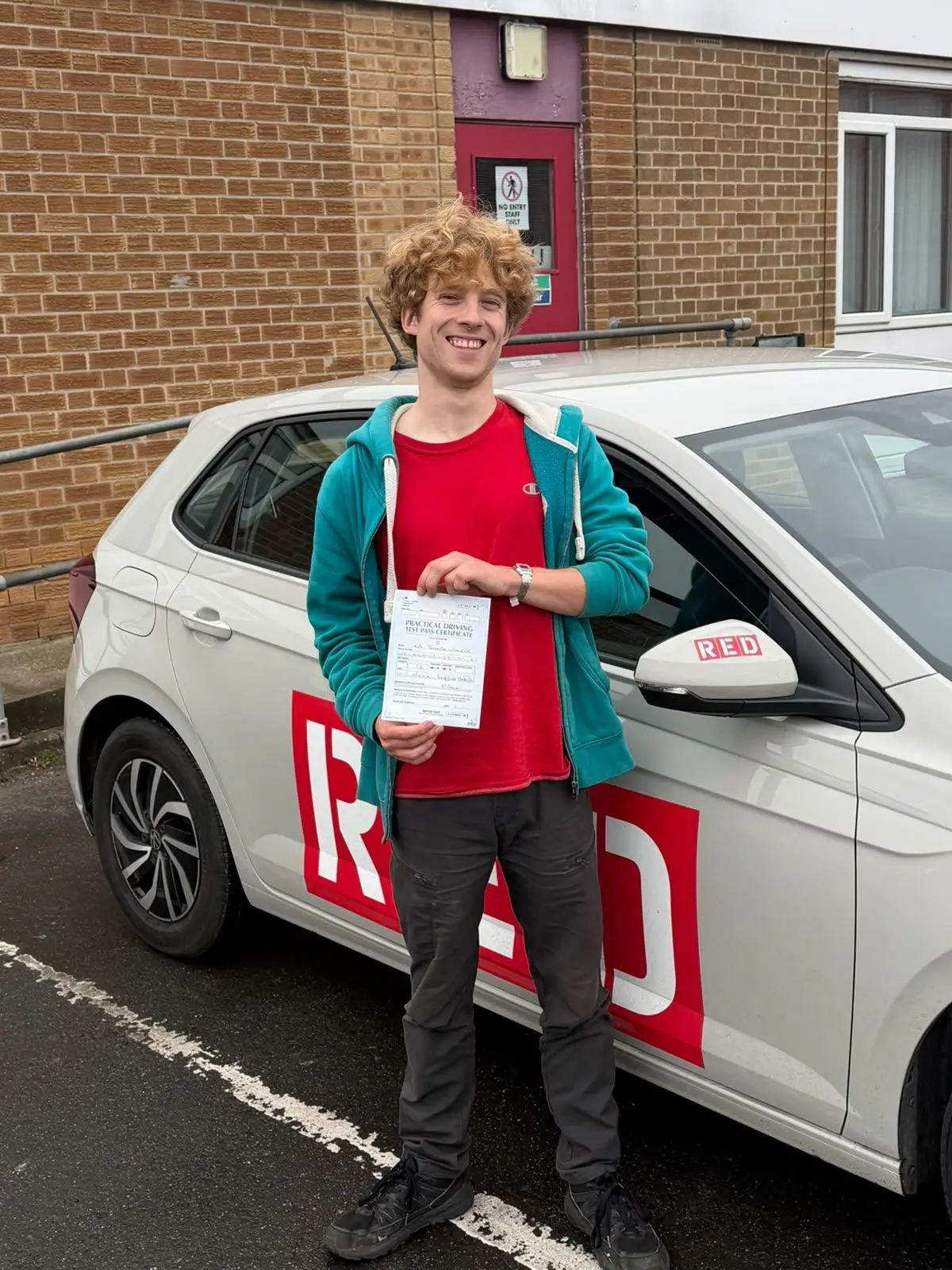 A learner holding their driving test pass certificate next to Mick&rsquo;s car
